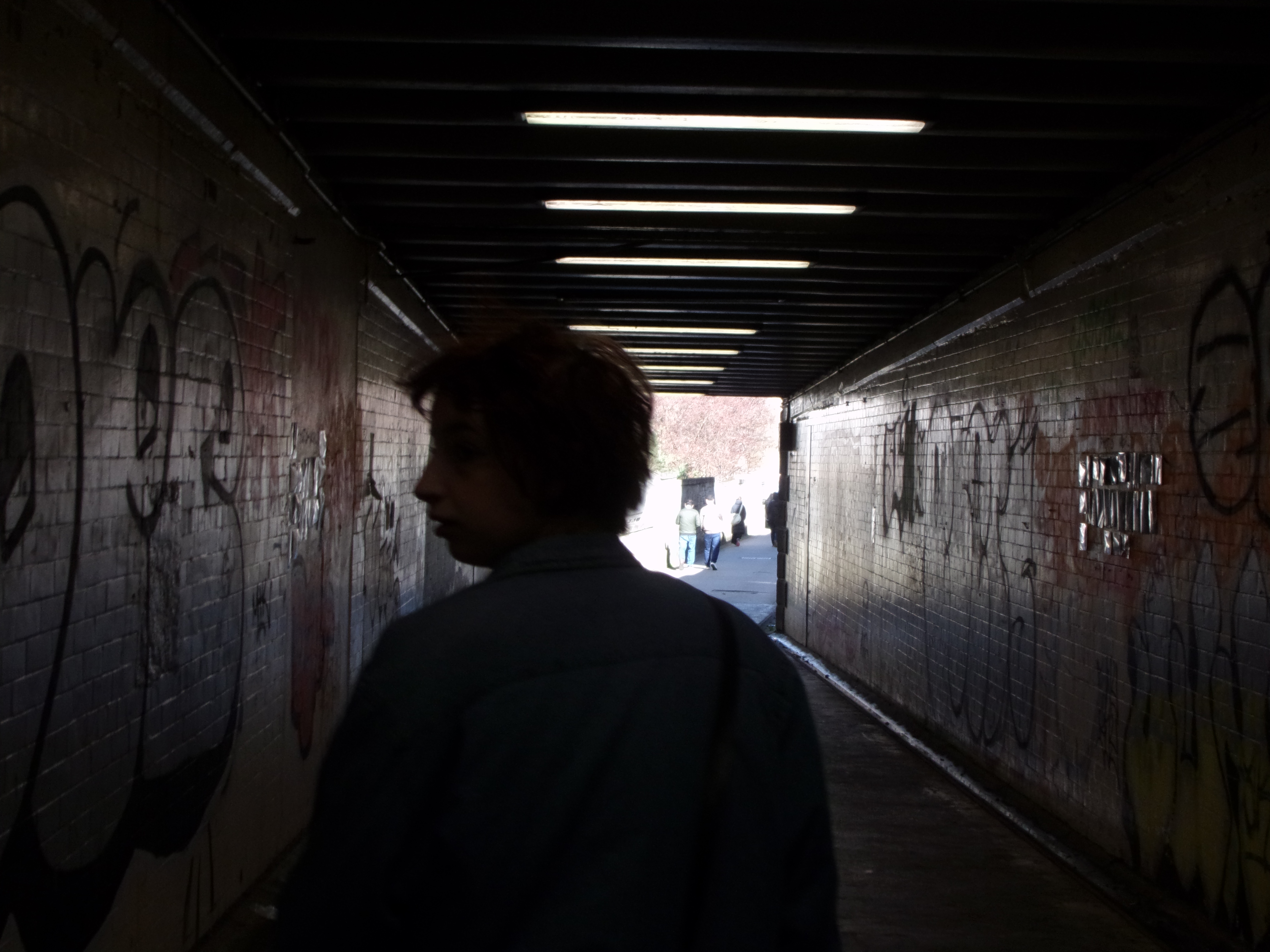 silhoutte view of a woman with a bob, back lit as they stand in a tunnel